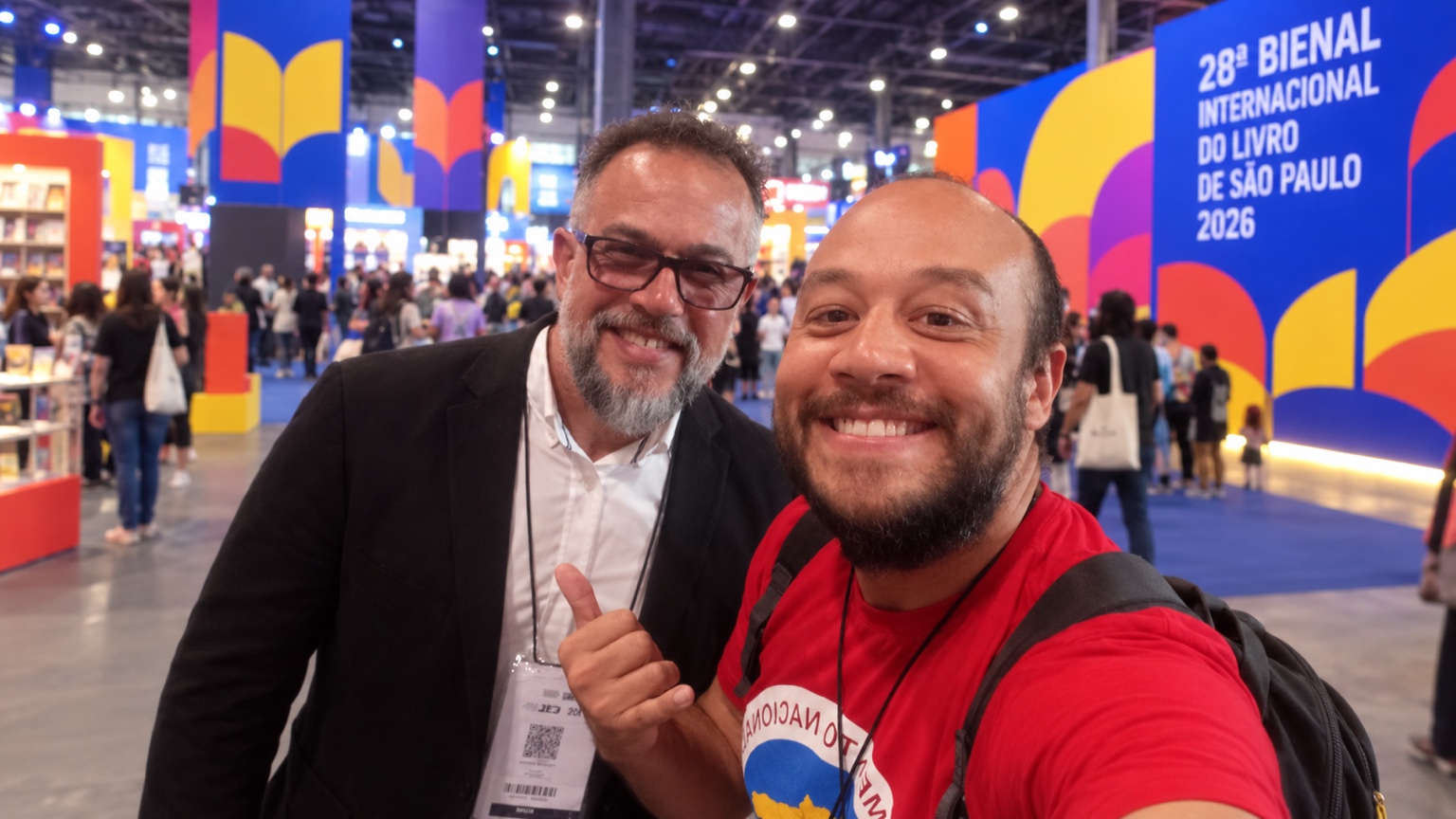 Carlos Toledo ao lado de outro autor participante, com o público e a identidade visual da 28ª Bienal Internacional do Livro de São Paulo ao fundo.
